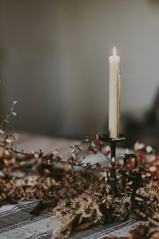Ett ensamt tänt ljus i en ljusstake omgiven av torkade blommor.